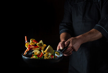 Cook prepares vegetables in a frying pan. Cooking healthy vegetarian food and meal on a dark background. Free advertising space.
