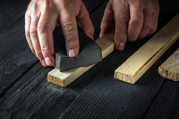 The woodworker cleans the wood plank with an abrasive tool. Builder hands close up. Renovation or construction idea