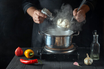 The chef prepares dumplings in a saucepan in the restaurant kitchen. Close-up - the hands of the cook add salt. Free ad space