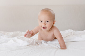 Crawling infant smiling while crawling on bed with white sheets