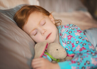 Sweet little red haired girl sleeping with stuffed bunny.
