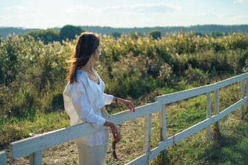 Woman relaxing on ranch and enjoying field view agricultural landscape in farm in sunset