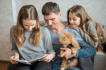 Dad with a dog and two daughters read a book together