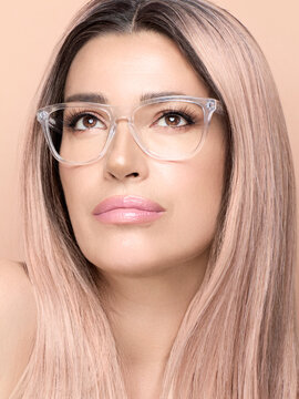 Beauty face woman with nude makeup wearing eyeglasses. Model with glasses looking up pensive. Close up portrait