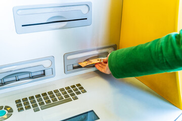 woman dressed in green coat taking out a 50 euro bill from an ATM