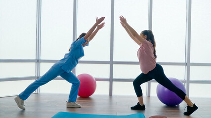 A Health Worker at a Medical Center Helps a Pregnant Woman to Do Exercises on a Ball with Dumbbells in Her Hands. The Expectant Mother Takes Care of her Health, Prepares for Childbirth.