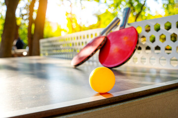 Street table tennis. Two tennis rackets with balls are on the ping pong table. Focus on the ball.