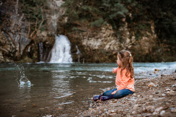 Girl throws stone into river in front of waterfall
