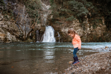 Small girl paddles by river in front of waterfall