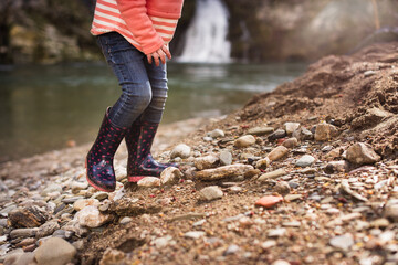 Girl's feet walking next to river over pebble beach