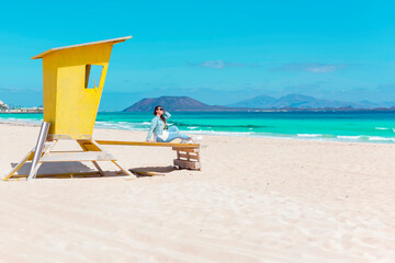 Young woman in sunglasses is on the yellow lifeguard tower on a beach