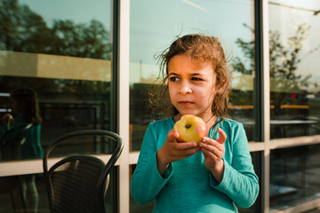 Young girl on restaurant patio eating. an apple