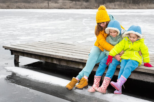 Mom with children sits on a wooden bridge by a frozen lake