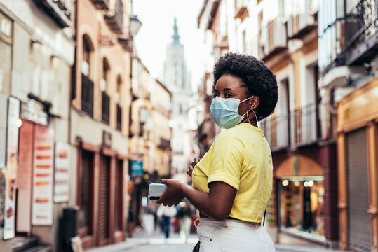 Portrait Of Black Girl With Face Mask, Afro Hair And Hoop Earrings Walking Down A Central Street Of The Old City.