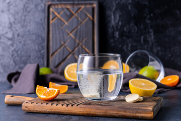 Glass with tasty drink, pills and citrus fruits on dark background