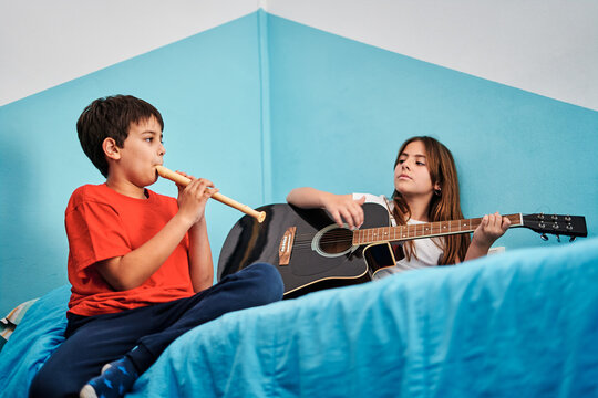 Boy and girl playing guitar and flute on top of bed in room
