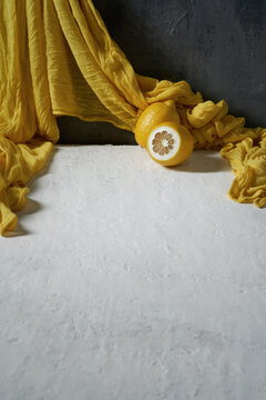 Two lemons and a yellow draped fabric on a white and gray background