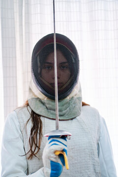Portrait of a young fencer girl with the mask and foil up in the middle of the face