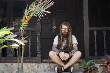 hipster guy with dreadlocks and tattoo sitting on the beach in thailan