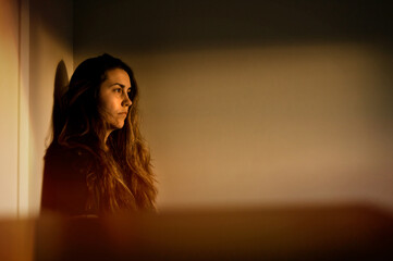 A woman standing in a bedroom watching the sunset from her window