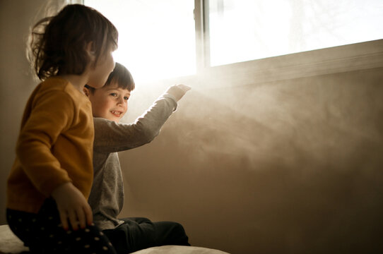 A brother and sister sitting on a bed watching rays of light