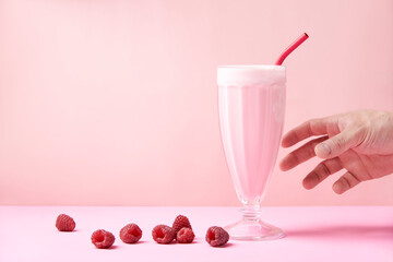 A hand grab a raspberry milkshake served in a glass with a reusable metal straw