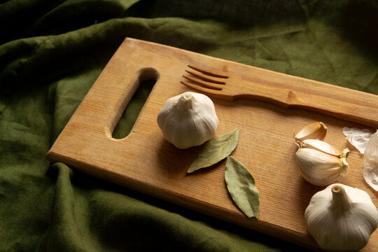 Garlic,bay leaf,wooden fork lie on cutting board on a green background