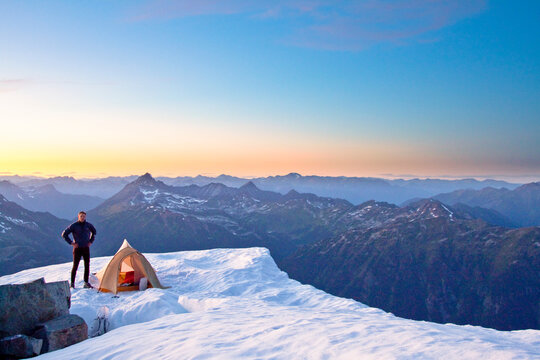 Climber standing next to tent on mountain summit, Whistler, Canada.