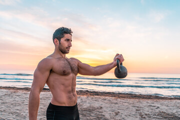 muscular man doing functional training with kettlebell on the beach at