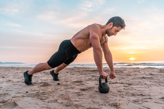 muscular man training core on the beach at sunrise