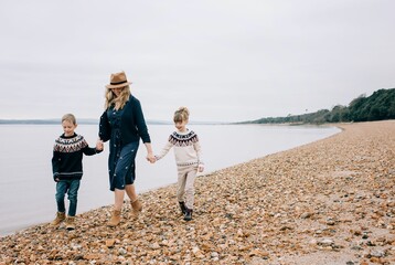 mom walking along the beach holding hands with her kids smiling