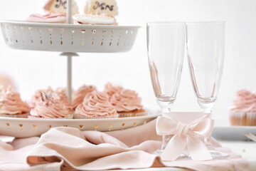 Glasses with ribbon and tasty wedding cupcakes on table