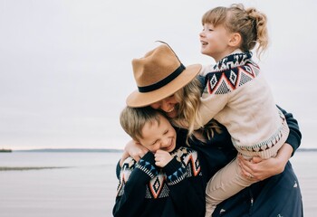 mom hugging her kids laughing whilst walking along the beach