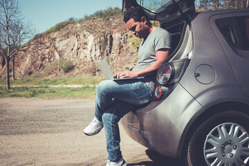 latino man searching on laptop for help sitting in back of car
