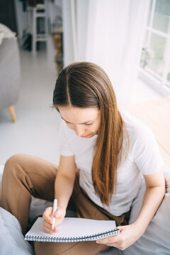 girl writes in a notebook and listens to music in bed
