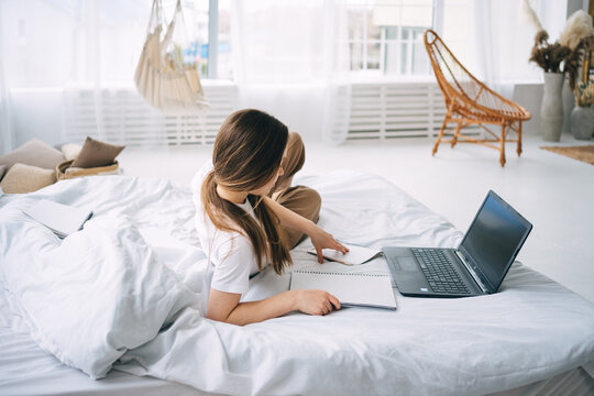 girl writes in a notebook and listens to music in bed