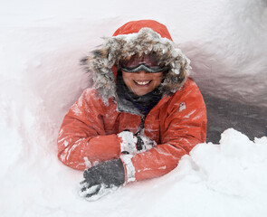 portrait of woman with faux fur hood and ski goggles in a snow hole