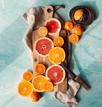 Slices of various citrus fruit on cutting board on blue background.