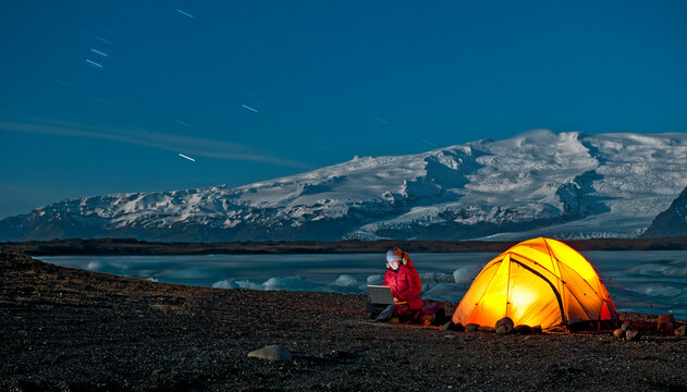 Scientist sits outside of her tent with laptop in Arctic climate
