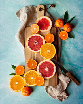 Slices Of Various Citrus Fruit On Cutting Board On Blue Background.