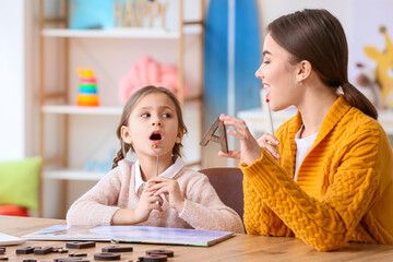 Speech therapist working with cute girl in clinic - obrazy, fototapety, plakaty