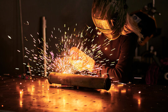 Female mechanic in protective helmet welding pieces