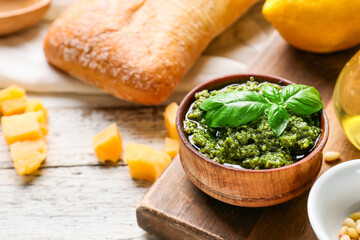 Bowl with tasty pesto sauce, bread and cheese on light wooden background, closeup