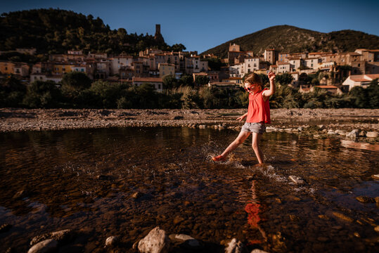 Girl splashes water in river in France with village in background