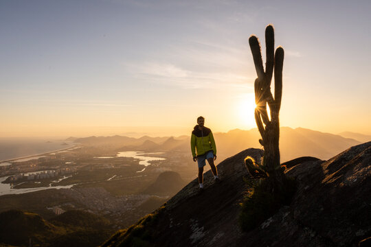 Man standing on rocky mountain edge next to big cactus on sunset