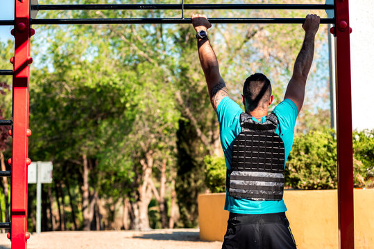 Rear view of Bearded brunette man doing a barbell pull-up with weight vest. Outdoor fitness concept.