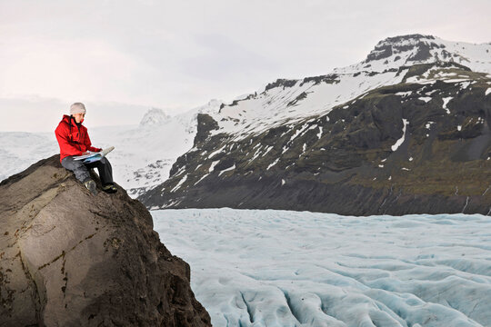 Female hiker reading map on rock above glacier