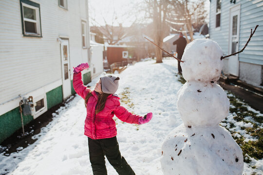 young girl poses with her snowman after a spring snowfall