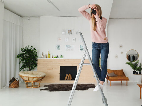 young blond female photographer making photo on the step-ladder