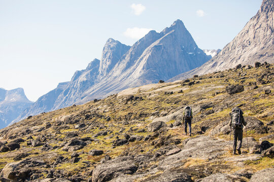 Two backpackers traverse an open talus slope below dramatic mountains.